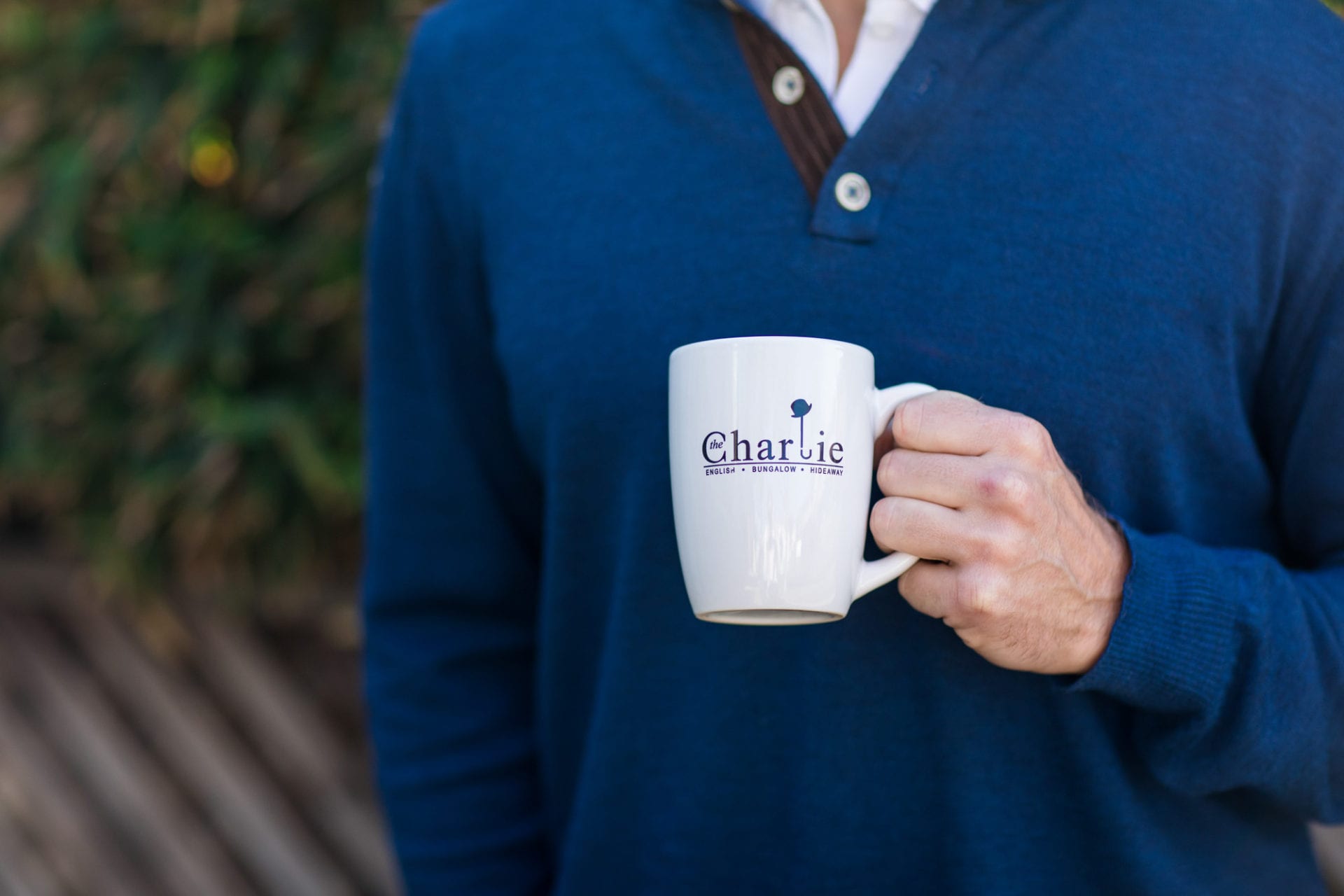 A man in a blue sweater, also known as The Charlie Hotel, holding a coffee mug.